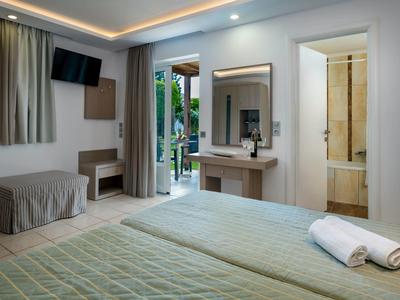 Nowoczesny pokój hotelowy z łóżkiem, telewizorem, biurkiem i balkonem z widokiem na zieleń.