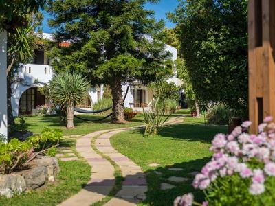Sentiero di pietra attraversa un giardino con alberi e fiori fino a una casa bianca.