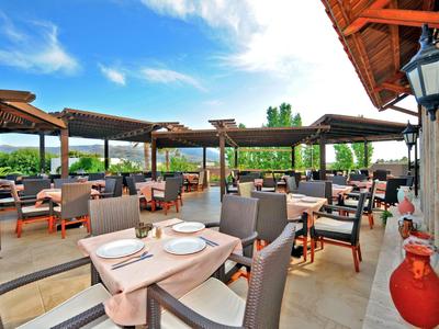 Freiluftrestaurant mit gedeckten Tischen und Blick auf grünes Gelände bei blauem Himmel.