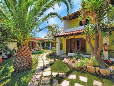 Haus im mediterranen Stil mit Garten, Palmen und sonnigem Weg zur Terrasse.