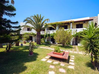 Hotelanlage mit zwei Stockwerken, grünen Garten und blauem Himmel im Hintergrund.