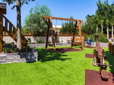 Grüner Garten mit Holzbänken, Schaukel und blauen Himmel, ideal für Urlaub oder Hotelaufenthalt.