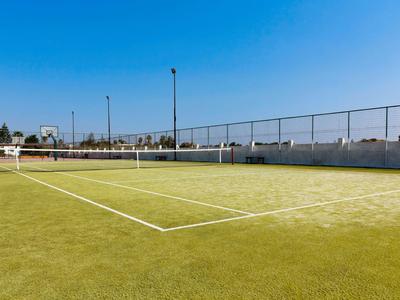 Leerer Tennisplatz mit grünem Kunstrasen unter klarem blauem Himmel.