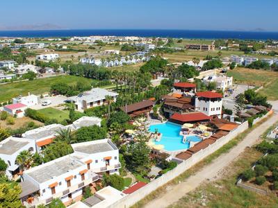 Ferienanlage mit Pool, umgeben von weißen Gebäuden, nahe Meer und landwirtschaftlichen Flächen.