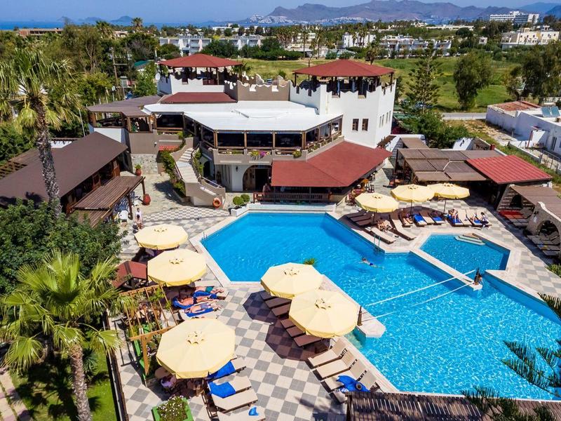 Widok z lotu ptaka na hotel z dużym basenem na zewnątrz, leżakami, parasolami i otaczającą zielenią.