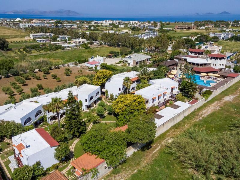 Widok z lotu ptaka na duży biały ośrodek z basenami i ogrodami blisko wody.