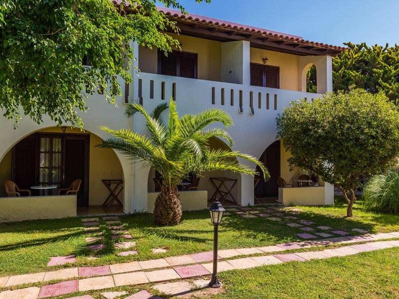 Dwupiętrowy biały budynek hotelowy z łukami, balkonem, palmą i zielonym trawnikiem