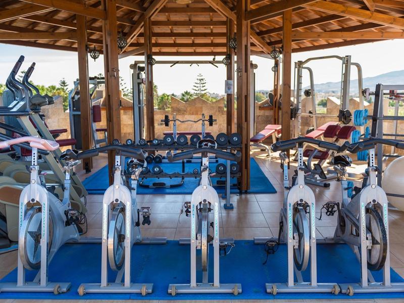 Wielofunkcyjna siłownia na świeżym powietrzu z rowerami stacjonarnymi i sprzętem do ćwiczeń pod drewnianą altaną.