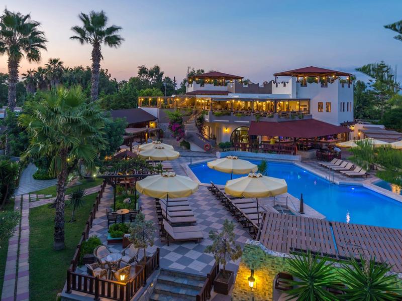 Luksusowy hotel z palmami i basenem na zewnątrz oświetlonym wieczorem.