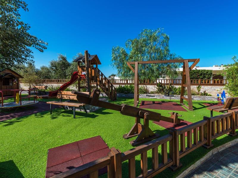 Słoneczny plac zabaw z drewnianymi konstrukcjami i zieloną sztuczną trawą.