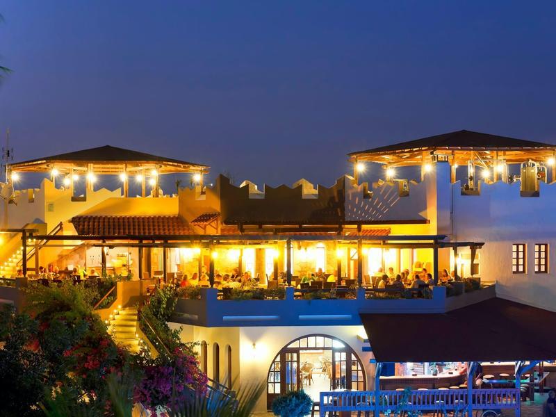 Oświetlony budynek hotelu o zmierzchu z zewnętrznym patio i ciepłym światłem.