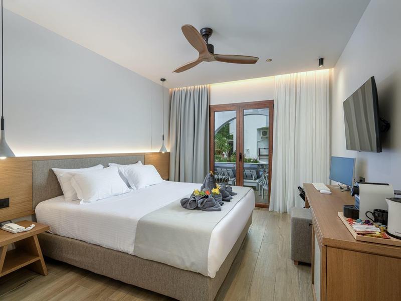 Nowoczesny pokój hotelowy z podwójnym łóżkiem, drewnianymi meblami i balkonem z widokiem na zewnątrz.