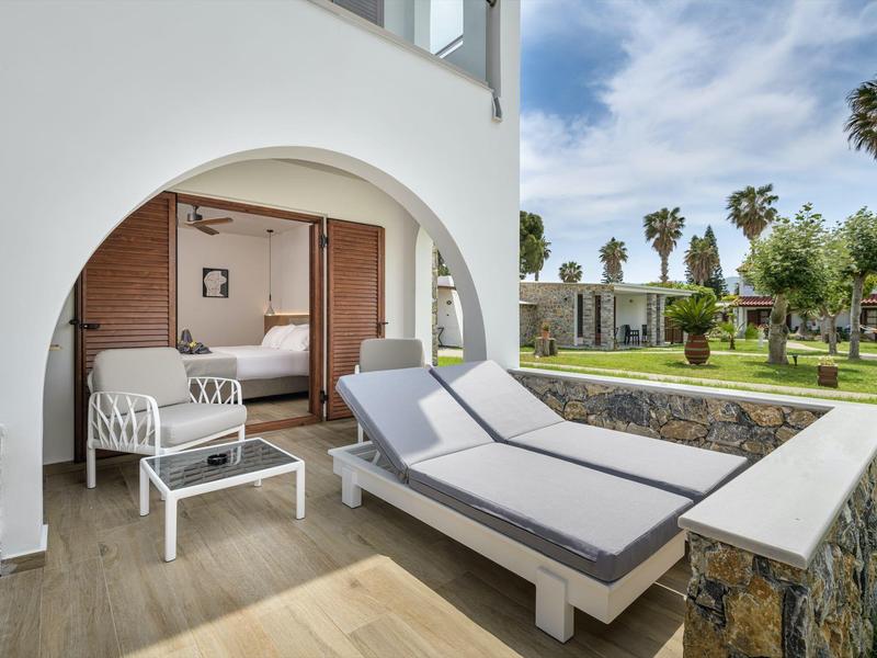 Balkon z leżakami z widokiem na ogród i palmy pod niebieskim niebem.