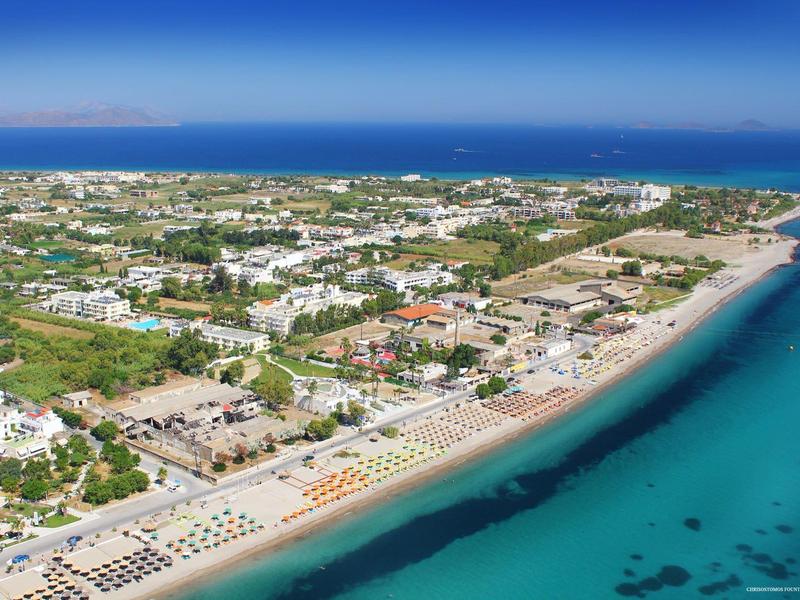 Widok z lotu ptaka na nadmorskie miasto z piaszczystą plażą, leżakami i jasną turkusową wodą.