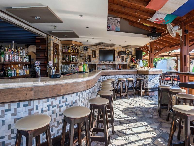 Słoneczny bar na świeżym powietrzu z drewnianymi stołkami, kafelkową podłogą i półką z alkoholem