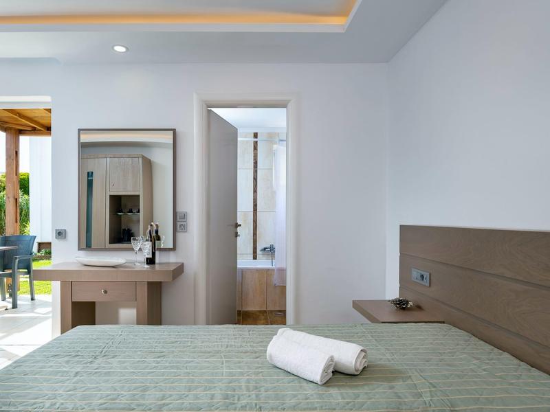 Nowoczesny pokój hotelowy z łóżkiem, zieloną narzutą, drewnianym biurkiem i otwartymi drzwiami do łazienki.