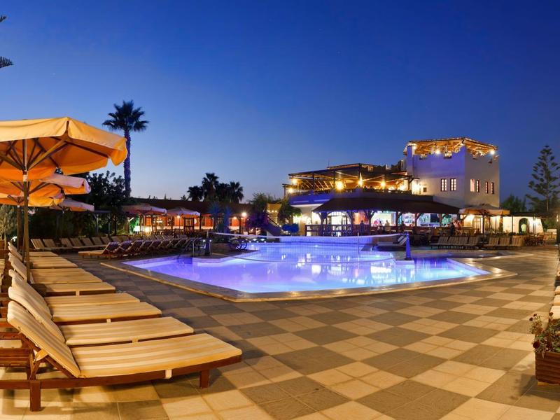 Strefa basenowa hotelu z leżakami i parasolami oświetlona o zmierzchu.