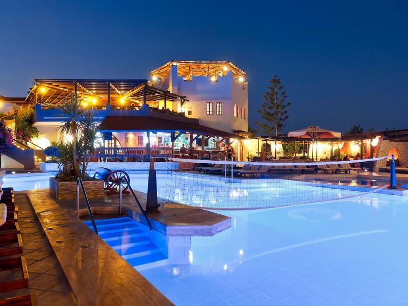 Oświetlony basen z leżakami i barem otoczony ciepłym światłem nocą.