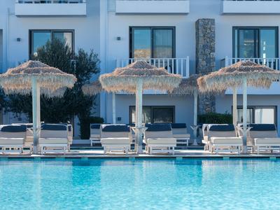 Piscina con lettini e ombrelloni di paglia davanti a un edificio di un hotel