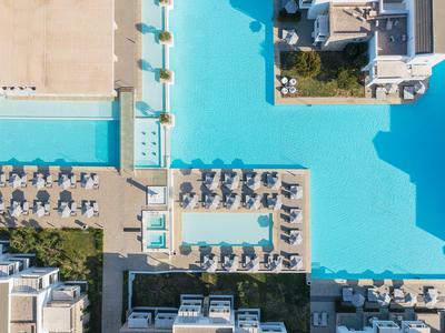 Vista aerea di una grande piscina limpida con lettini e ombrelloni in un hotel.