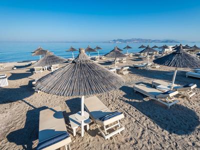 Beach with sun loungers and straw umbrellas by calm blue sea under clear sky