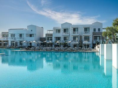 Complesso alberghiero moderno con grande piscina e lettini sotto un cielo azzurro.