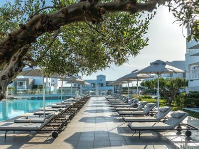 View of a modern hotel pool with sun loungers and umbrellas under trees.