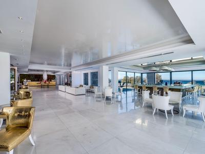 Bright, modern hotel lobby area with white marble floor and seating groups overlooking the sea.