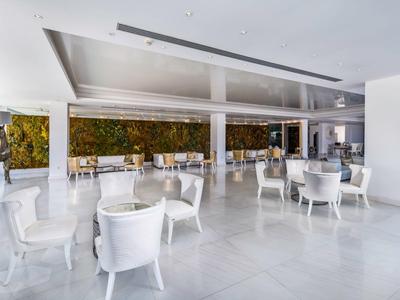 Bright hotel lobby area with white chairs and tables on marble floor and green wall decoration.
