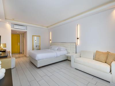 Bright hotel room with double bed, sofa, TV, and modern decor.