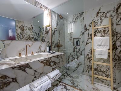 Luxury bathroom with marble walls, double sinks, and a wooden ladder towel rack.