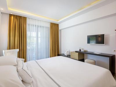 Modern hotel room with large bed, TV, and balcony with curtains.