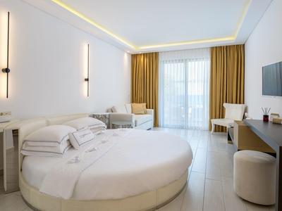 Modern hotel room with round bed, yellow curtains, and bright walls.