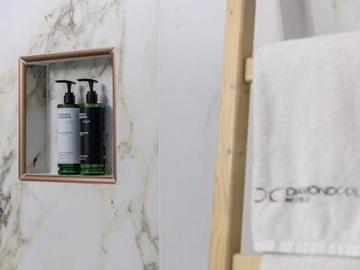 Two bottles of liquid soap in a marble niche, next to a wooden rack with a white towel.