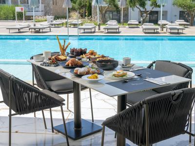 Table with various foods and drinks next to a pool with lounge chairs in the background.
