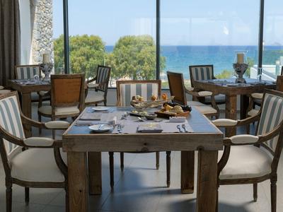 A restaurant with wooden tables and chairs overlooking the sea through large windows.