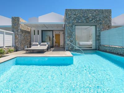Modern pool in front of a luxurious villa under clear sunny skies.