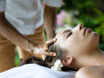 Woman receiving a relaxing head massage outdoors in a peaceful setting.