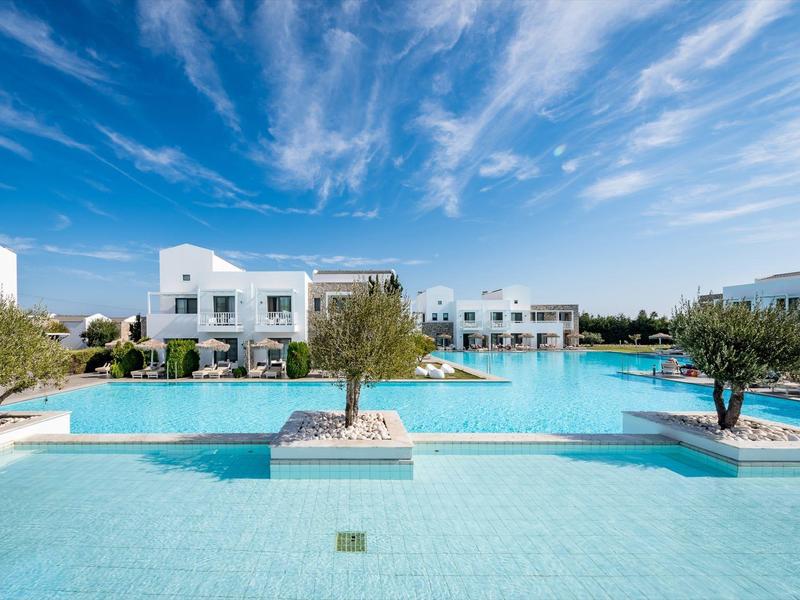Modern hotel complex with large pool and white buildings under blue sky