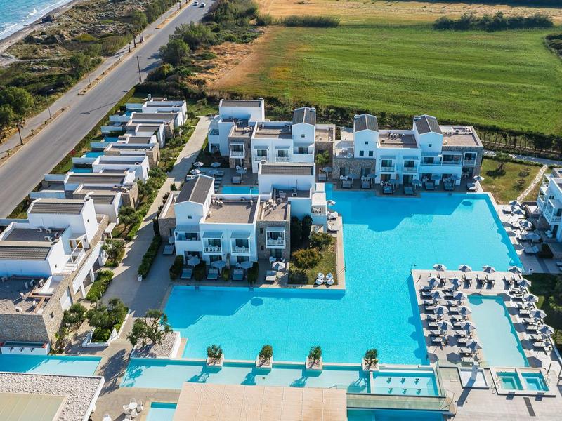 Aerial view of a resort with large pool, white buildings, and adjacent beach.