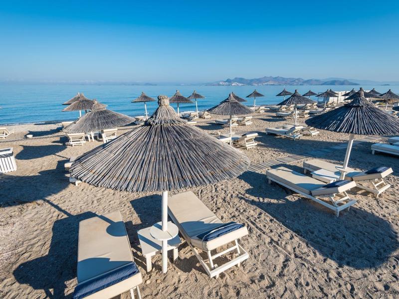 Beach with sun loungers and straw umbrellas by calm blue sea under clear sky