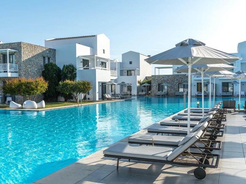 Modern hotel pool with lounge chairs and white umbrellas beside white buildings.
