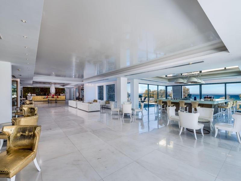 Bright, modern hotel lobby area with white marble floor and seating groups overlooking the sea.