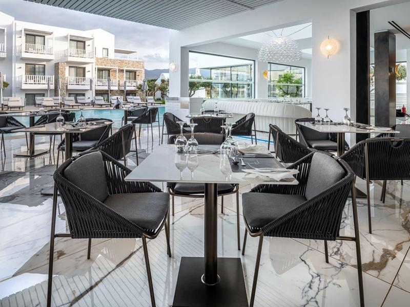 Modern, elegant restaurant with chairs and tables, large windows, and bright marble flooring.