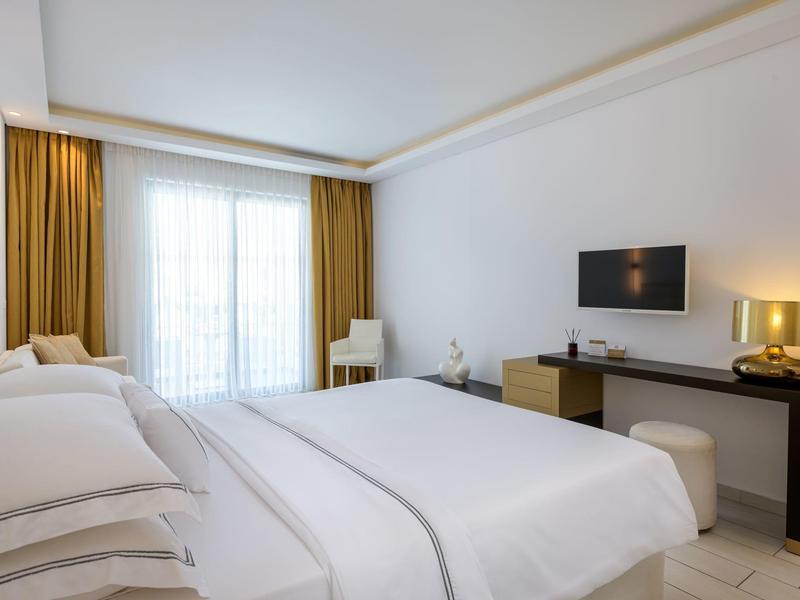 Modern hotel room with large bed, desk, and balcony window with curtains.
