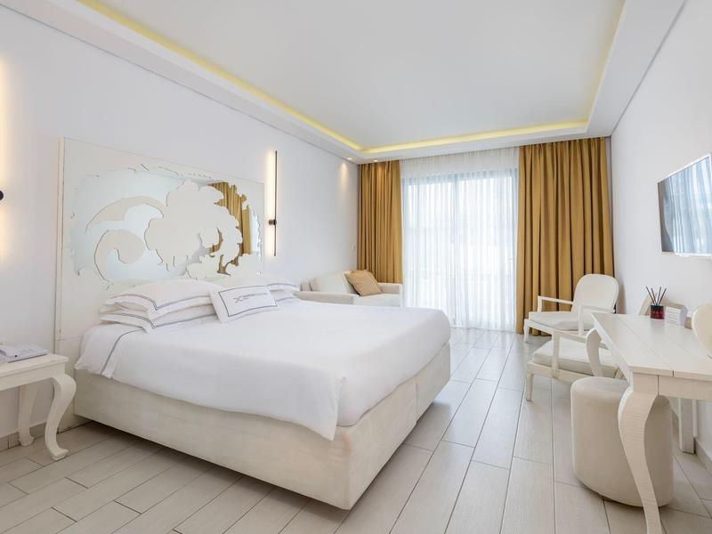 Bright hotel room with large bed, white furniture, and gold curtains.
