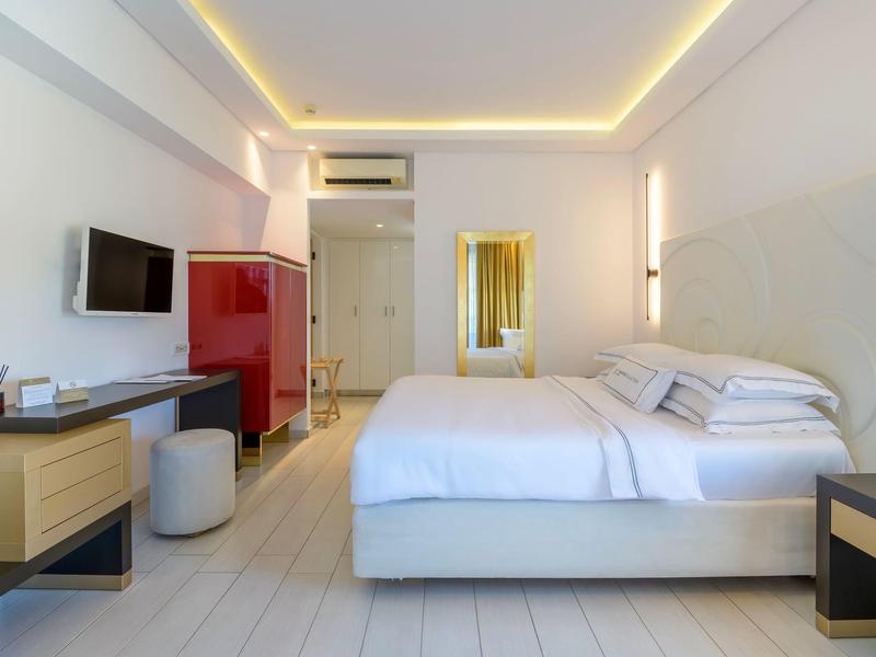 Modern hotel room with large bed, white decor, and indirect ceiling lighting.
