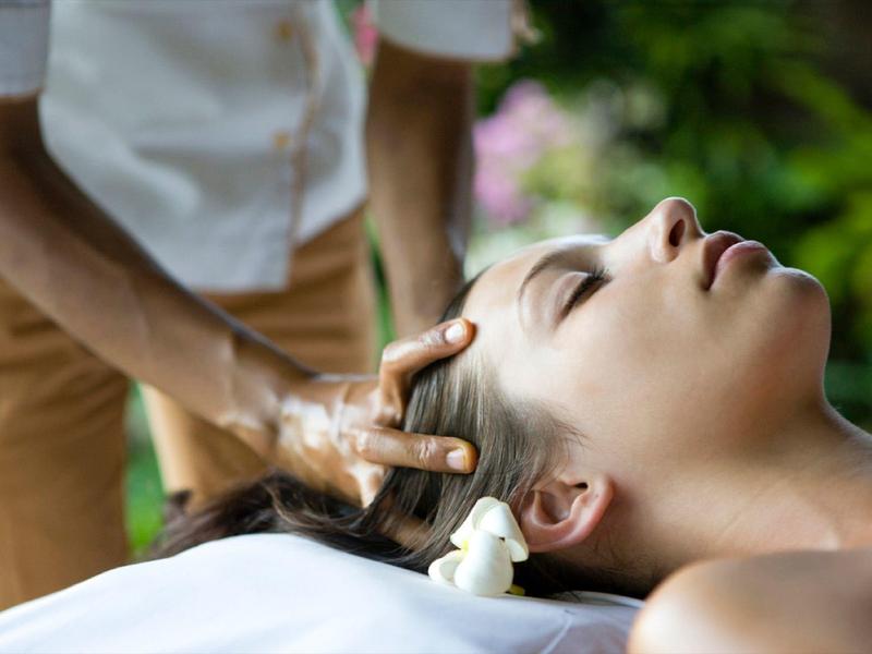 Woman receiving a relaxing head massage outdoors in a peaceful setting.