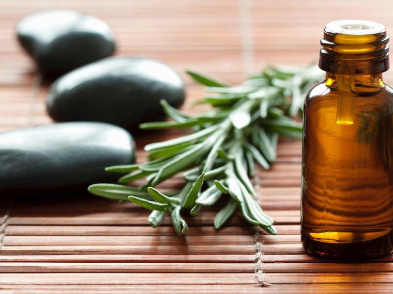 Brown essential oil bottle next to green leaves and black stones on bamboo mat