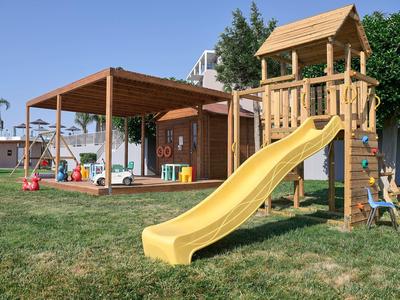 Kinderspielplatz mit gelber Rutsche, Holzturm, Schaukel und überdachtem Bereich auf grünem Rasen.